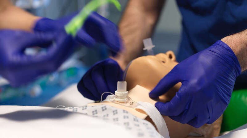 Photograph of a tracheotomy tube on a mannequin with medical-gloved hands in shot 